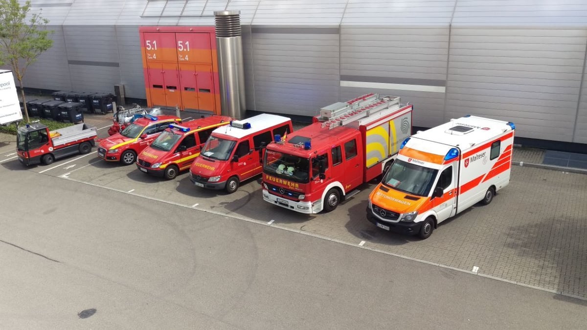 Reihe verschiedener Einsatzfahrzeuge von Feuerwehr und Rettungsdienst auf einem Parkplatz vor einer Halle.