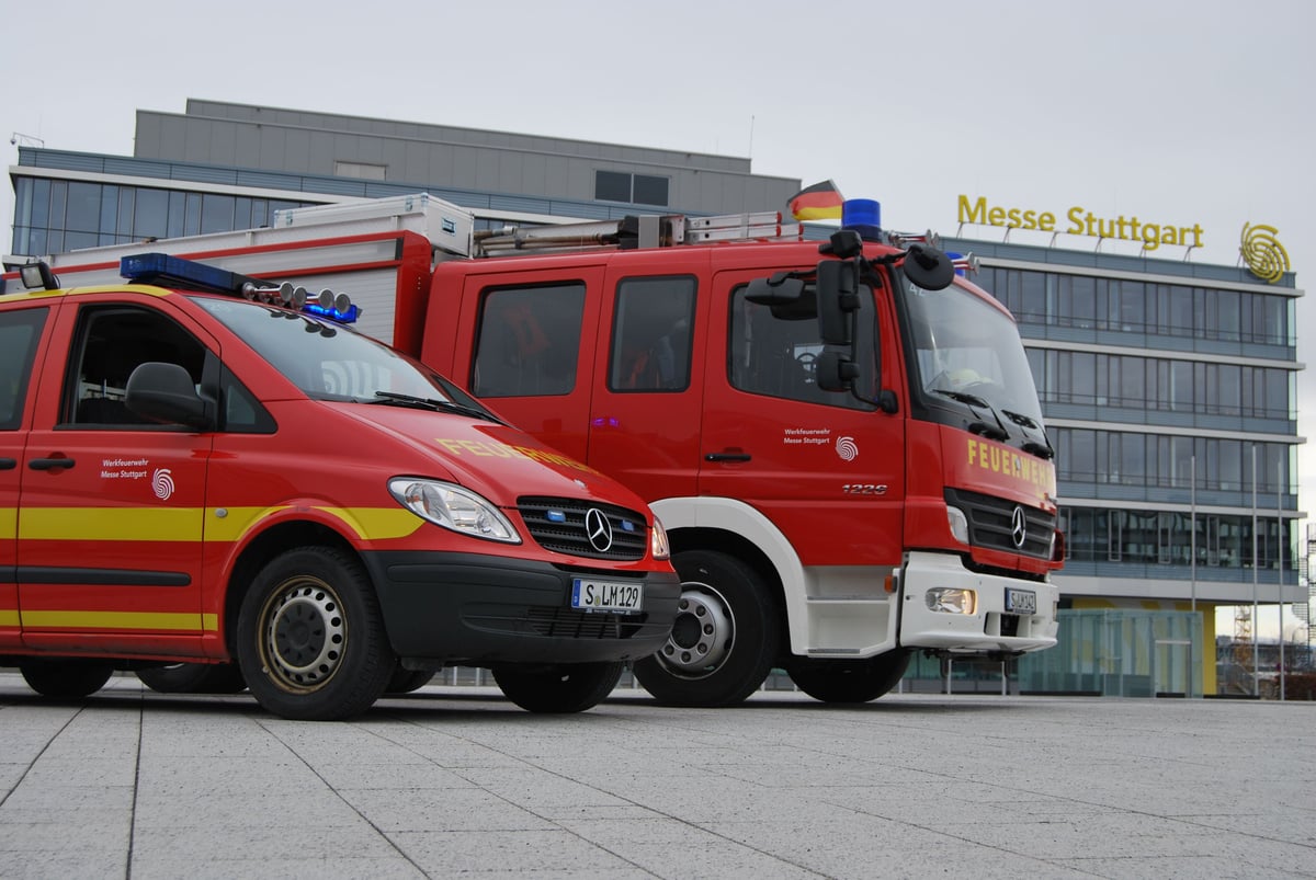 Zwei rote Einsatzfahrzeuge der Werkfeuerwehr Messe Stuttgart stehen vor dem Messegebäude.