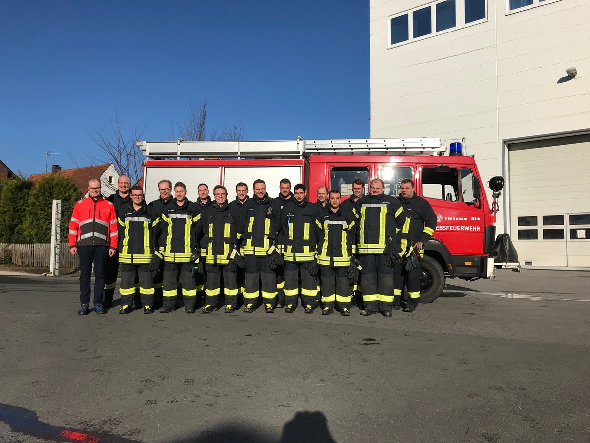 Gruppenfoto der Betriebsfeuerwehr in Einsatzkleidung vor einem roten Feuerwehrfahrzeug.