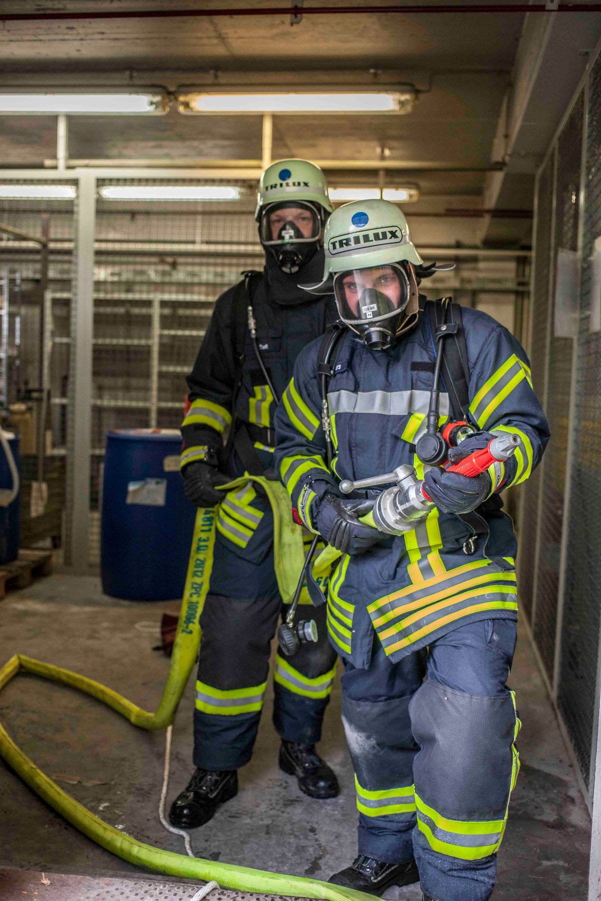 Zwei Feuerwehrkräfte der Betriebsfeuerwehr TRILUX mit Atemschutzmasken halten einen Druckschlauch.