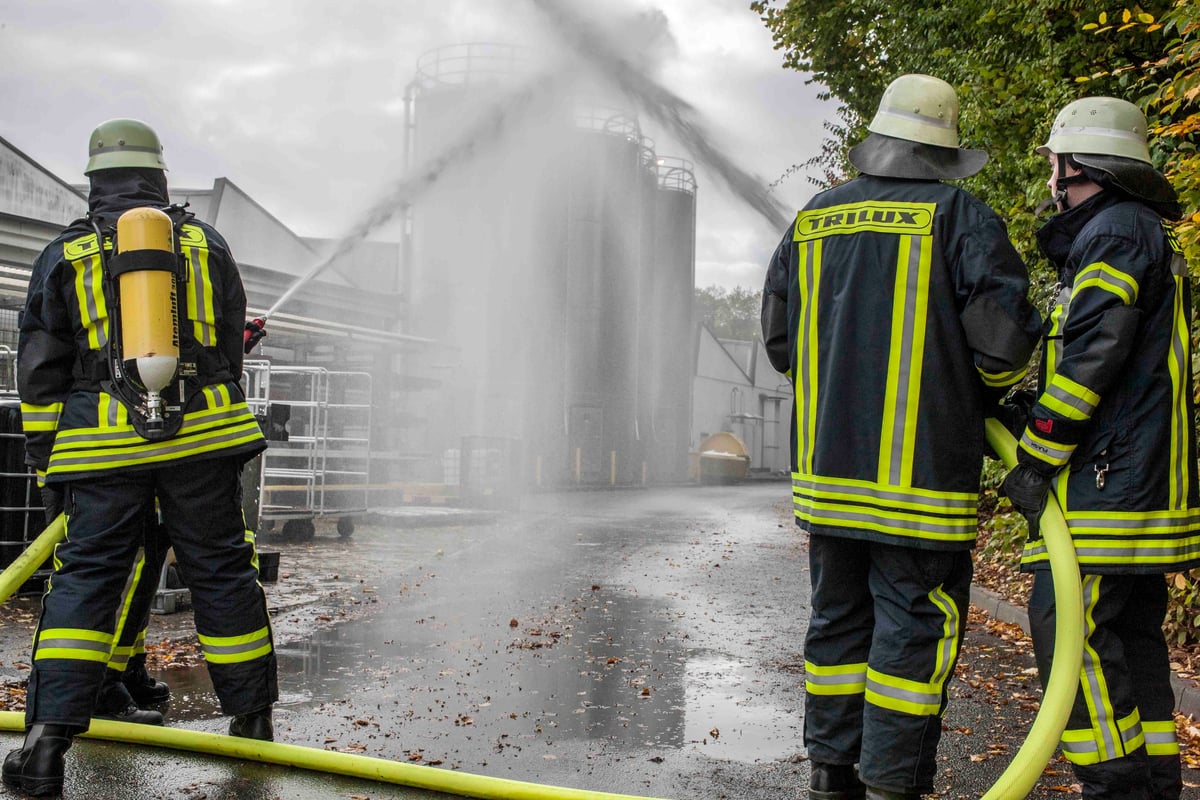 Feuerwehrleute der Betriebsfeuerwehr TRILUX bei einer Löschübung mit Wasserschläuchen auf einem Betriebsgelände.