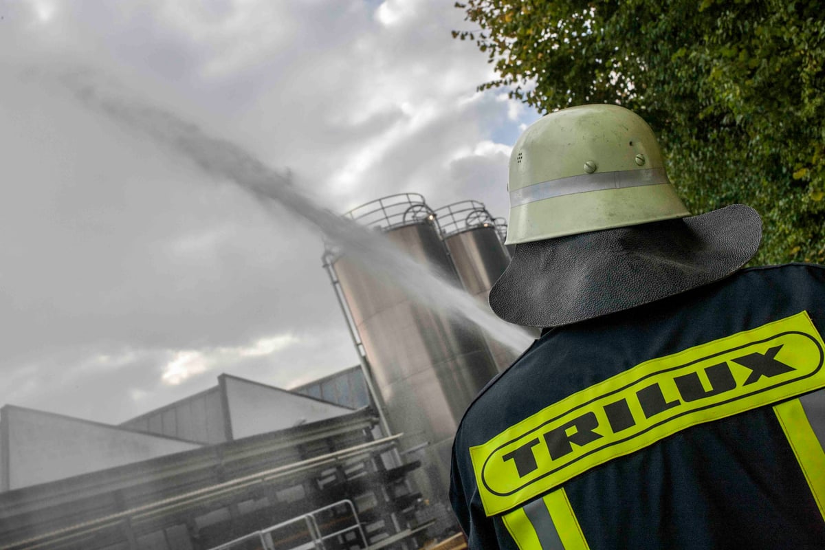 Mitglied der TRILUX-Betriebsfeuerwehr sprüht bei einer Übung Wasser auf große Metallsilos.