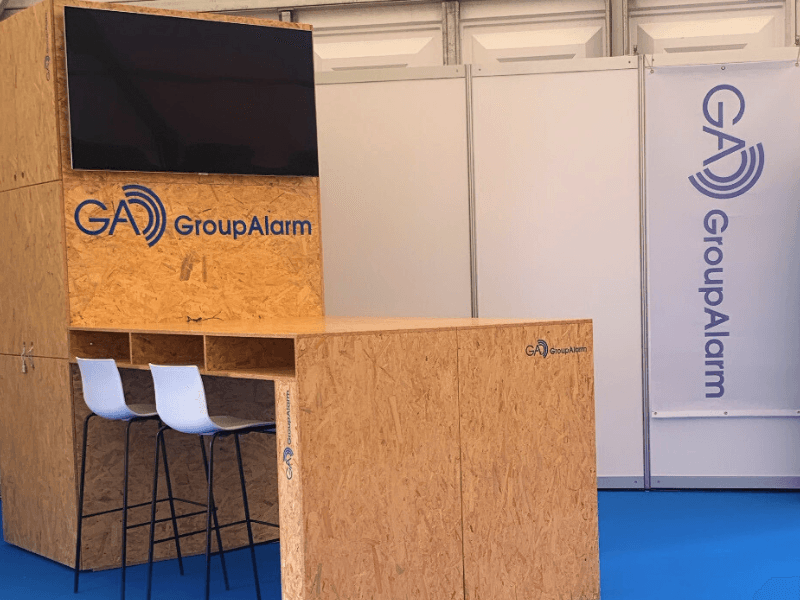 Messestand von GroupAlarm mit Holztheke und Monitor.
